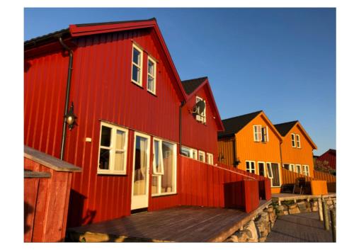 a row of red buildings with a wooden deck at Ballstad Brygge Rorbu in Ballstad