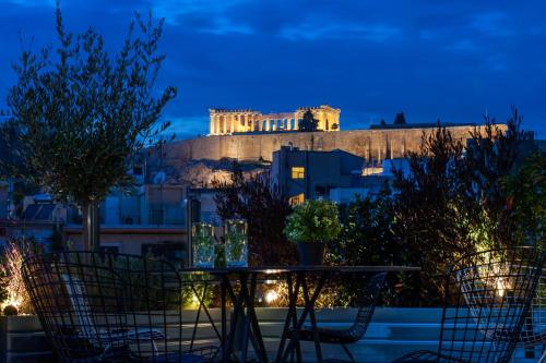 a table and chairs in front of the acropolis at night at B4B Athens Signature Hotel in Athens