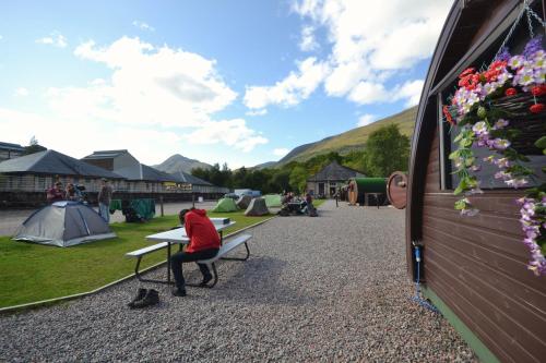a person sitting on a bench next to a group of tents at Blackwater Glamping Pods in Kinlochleven