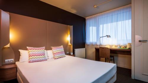 um quarto com uma cama branca com almofadas e uma secretária em Campanile Hotel & Restaurant Amsterdam Zuid-Oost em Amsterdã