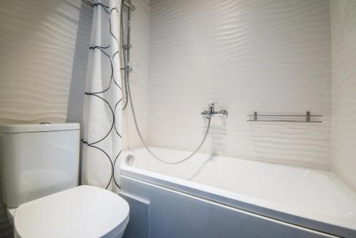a white bathroom with a toilet and a bath tub at Sunshine Apartment in Liepāja