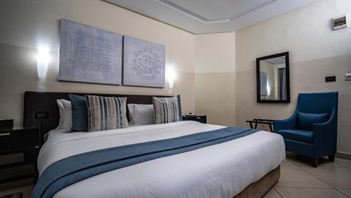 a bedroom with a large bed and a blue chair at Oak Plaza Hotels East Airport in Accra