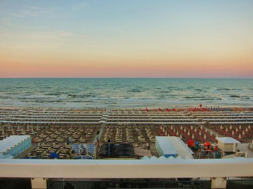 a beach with chairs and the ocean at sunset at Hotel Cigno D'Oro in Riccione