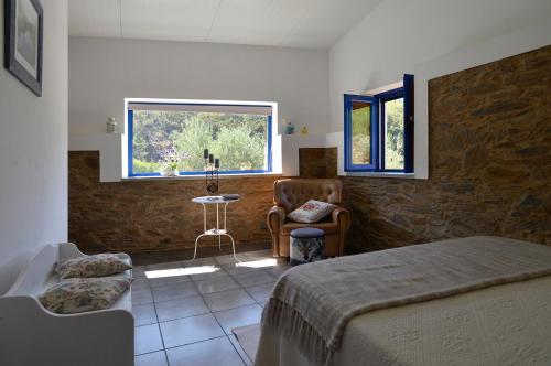 a bedroom with a bed and a chair and a window at REFÚGIO DO RAPOSO/CASA DA RIBEIRA (AGROTURISMO) in Proença-a-Nova