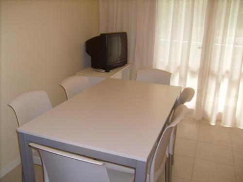 Habitación con mesa blanca, sillas y TV. en Condominio Rio Chico, en Lignano Sabbiadoro