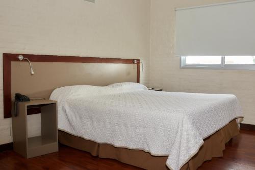 a bedroom with a bed with a white comforter and a window at Hotel Juana de Ibarbourou in Melo