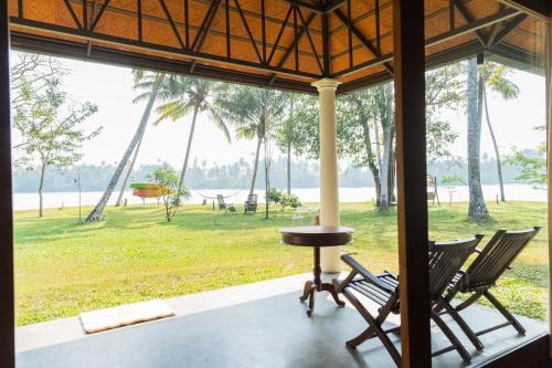 a porch with chairs and a table and a view of a park at Cranganor History Café & Riverside Château in Parūr