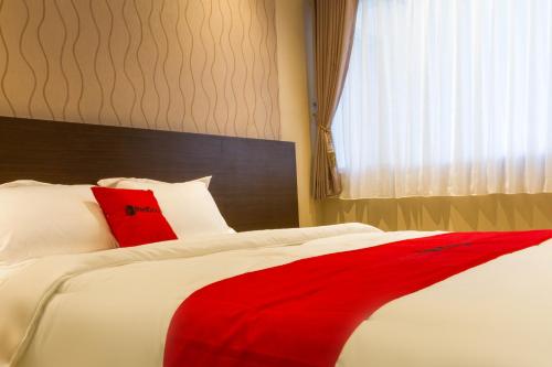 a red blanket on a white bed with a window at RedDoorz Plus @ Dipatiukur in Bandung