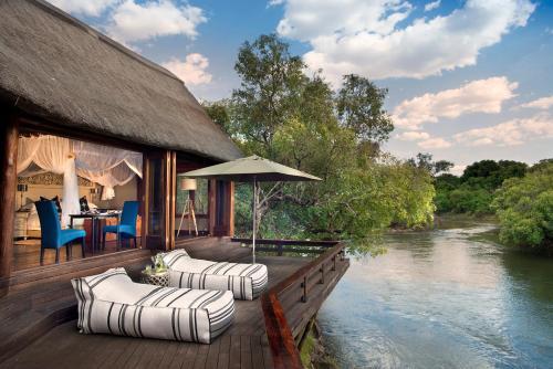 ein Haus mit einer Terrasse mit Stühlen und einem Fluss in der Unterkunft Royal Chundu Island Lodge in Livingstone