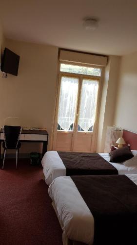 a hotel room with two beds and a desk and a window at Hotel Au Val Doré in La Bourboule