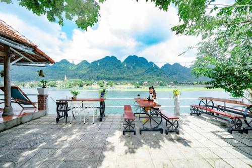 a woman sitting at a table near the water at Areca Bungalow in Phong Nha