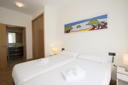 een slaapkamer met een wit bed met een foto aan de muur bij The Rentals Collection | Avenida II in San Sebastian