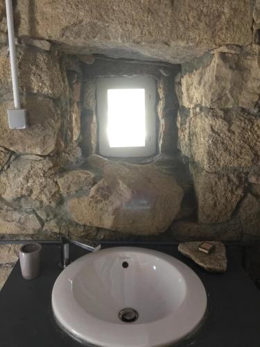 La salle de bains en pierre est pourvue d'un lavabo et d'une fenêtre. dans l'établissement Casetta, à Olivese
