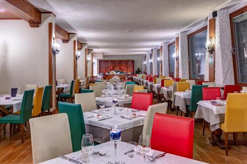 a restaurant with white tables and colorful chairs at Hotel Mondolé - Azzurro Club in Prato Nevoso