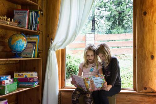 two young girls sitting in a window looking at a book at CHATA PACHNĄCA LASEM in Andrychów