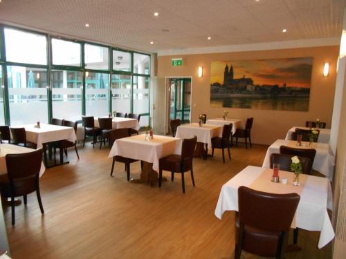 um restaurante com mesas e cadeiras brancas e janelas em Síu Hotel Magdeburg em Magdeburg