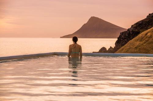 a woman sitting in a bath tub looking out at the ocean at Hvammur 2 Bjarg with private hot tub in Drangsnes