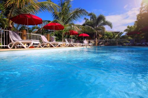 a swimming pool with chairs and red umbrellas at Résidence Oasis de Terre Rouge in Saint-Pierre