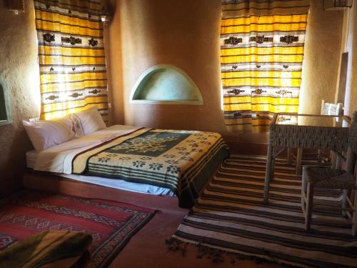 a bedroom with a bed and a table and windows at Casbah d'hôte La Jeanne Tourisme Ecologique in Boumalne Dades