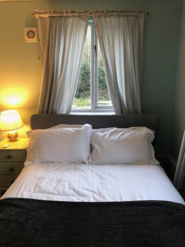 a bed with white pillows in front of a window at Fossewold Cotswold Barn in Chipping Campden