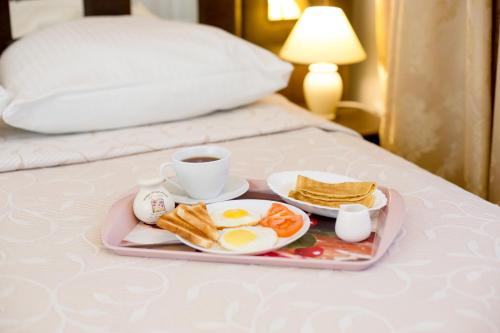a breakfast tray with eggs and toast and coffee on a bed at Гостиница Бастон на Герцена in Tomsk