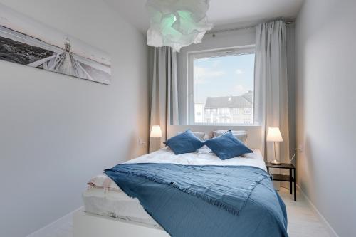 sypialnia z łóżkiem z niebieskimi poduszkami i oknem w obiekcie NORDBYHUS Apartamenty Nowa Grobla w Gdańsku
