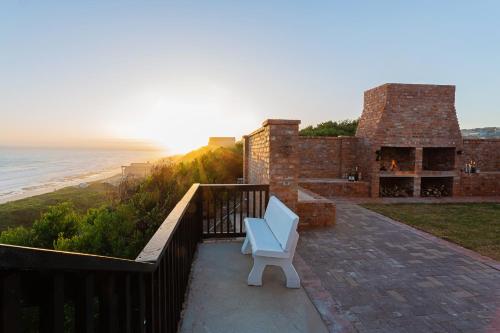 a white bench sitting on a balcony overlooking the beach at Seeplaas Guesthouse in Groot Brak Rivier