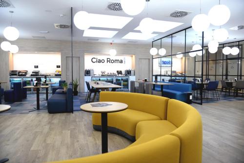 a lobby with a yellow couch and tables and chairs at Air Rooms Rome Airport by HelloSky in Fiumicino