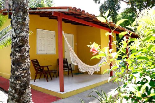 a porch of a yellow house with a hammock at Pousada Pérola do Atlântico in Ilha de Boipeba