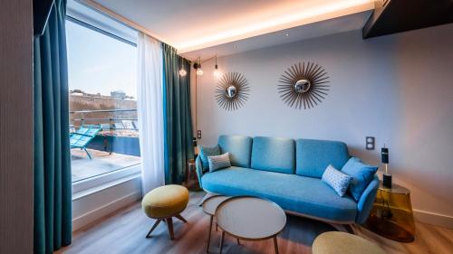 a living room with a blue couch and a large window at voco Strasbourg Centre - The Garden by IHG in Strasbourg
