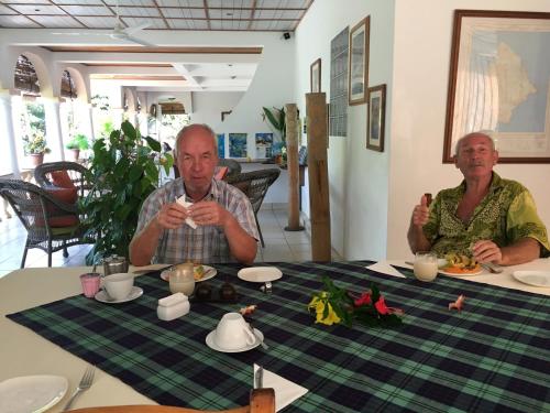 Zwei Männer sitzen an einem Tisch und trinken Tee. in der Unterkunft Chalets de Palma in La Digue