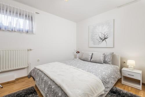 a white bedroom with a bed and a window at Apartman Javor in Otočac