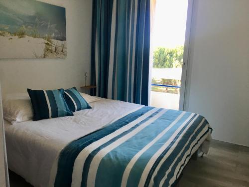 um quarto com uma cama com lençóis azuis e brancos e uma janela em RESIDENCE DE LA MER em Le Grau-du-Roi