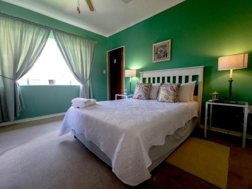 a bedroom with a bed with green walls and a window at Loerie Guesthouse in Hoedspruit
