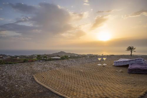 una manta y copas de vino en una playa con puesta de sol en Dammuso Sant'Anna, en Pantelleria