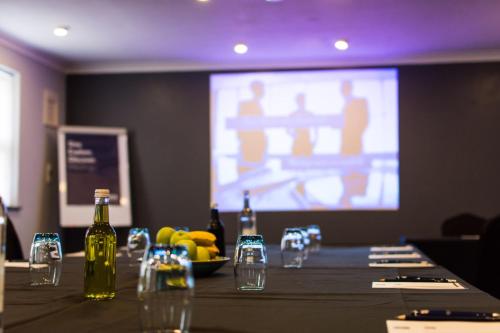 a long table with bottles and glasses and a screen at Dragonfly Hotel King's Lynn in Kings Lynn