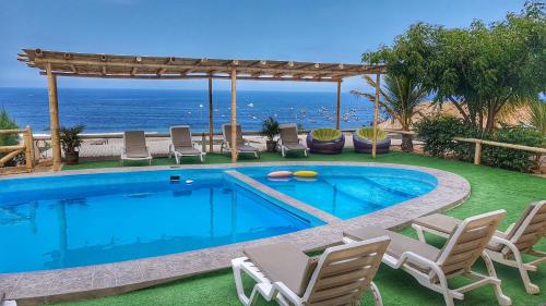 a swimming pool with chairs and the ocean in the background at El Gran Velero in Los Órganos