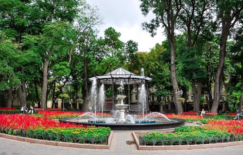 a fountain in the middle of a park with red flowers at Langery Residence Central Apartments in Odesa