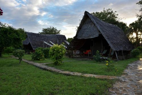 two huts with thatched roofs on the grass at Bahari Pori Resort in Pangani