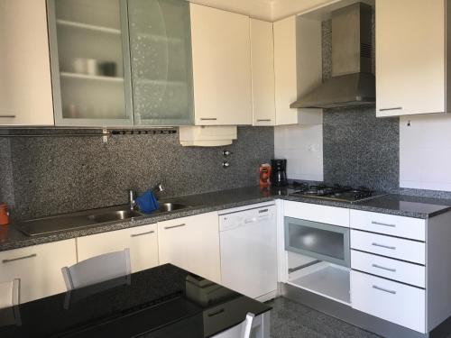 a kitchen with white cabinets and black counter tops at Apartamento novo muito confortável com vista Rio in Algés