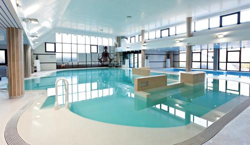 a large pool with blue water in a building at Thalazur Ouistreham - Hôtel & Spa in Ouistreham