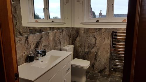 Un baño con lavabo e inodoro y dos ventanas. en Criffel Cottage, en Dumfries