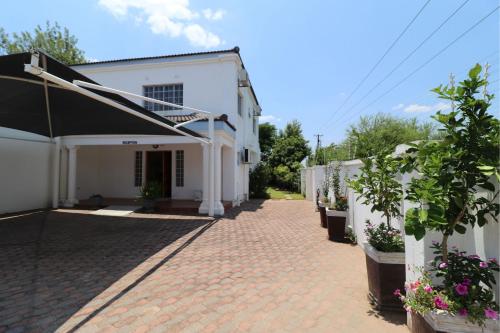 a white building with potted plants on a brick sidewalk at Sentosa Guest House in Francistown