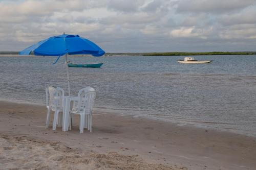 two chairs and an umbrella on a beach with a boat at Pousada o Forte in Mangue Sêco