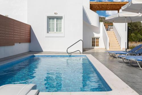 a pool with chairs and an umbrella next to a building at Milos Villas Complex in Pefki Rhodes