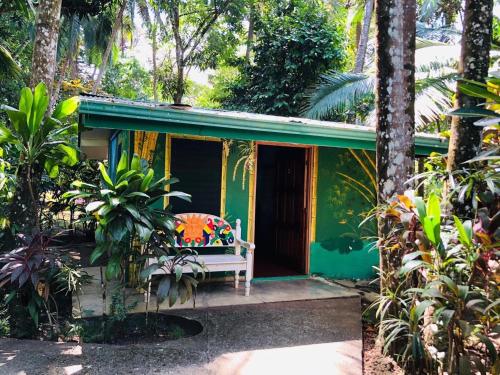 a green house with a bench in front of it at Chosa Manglar Suites & Cabins in Puerto Jiménez
