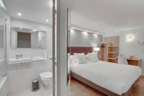 a bedroom with a white bed and a bathroom at Hôtel l'Amandier in Nanterre