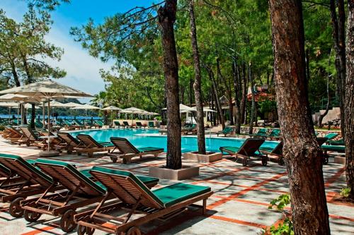 a pool with chairs and umbrellas and trees at Marti Hemithea Hotel in Orhaniye