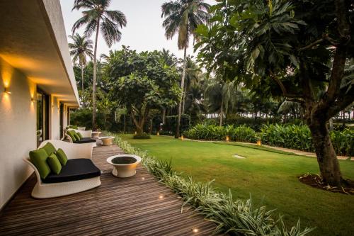 eine Holzterrasse mit Stühlen und eine Liegewiese mit Palmen in der Unterkunft Planet Hollywood Beach Resort Goa in Utorda