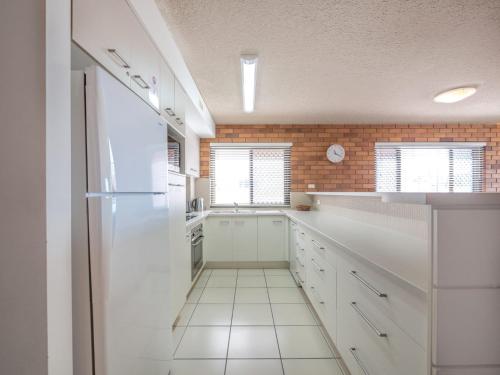 a kitchen with white cabinets and a brick wall at San Clemente 3 24 Orvieto Tce in Caloundra